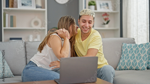 Beautiful couple using laptop sitting on sofa hugging each other at home