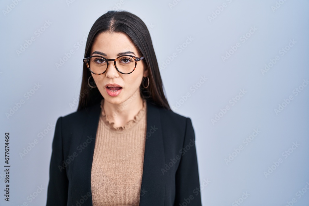 Young brunette woman standing over blue background afraid and shocked with surprise expression, fear and excited face. Young brunette woman standing over blue background afraid and shocked with surprise expression, fear and excited face.