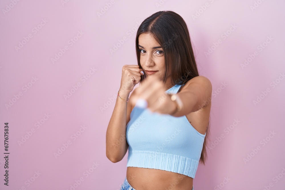 Young brunette woman standing over pink background ready to fight with fist defense gesture, angry and upset face, afraid of problem Young brunette woman standing over pink background ready to fight with fist defense gesture, angry and upset face, afraid of problem