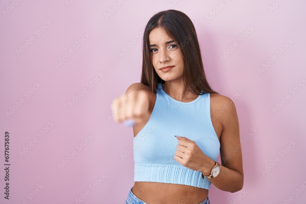 Young brunette woman standing over pink background punching fist to fight, aggressive and angry attack, threat and violence Young brunette woman standing over pink background punching fist to fight, aggressive and angry attack, threat and violence