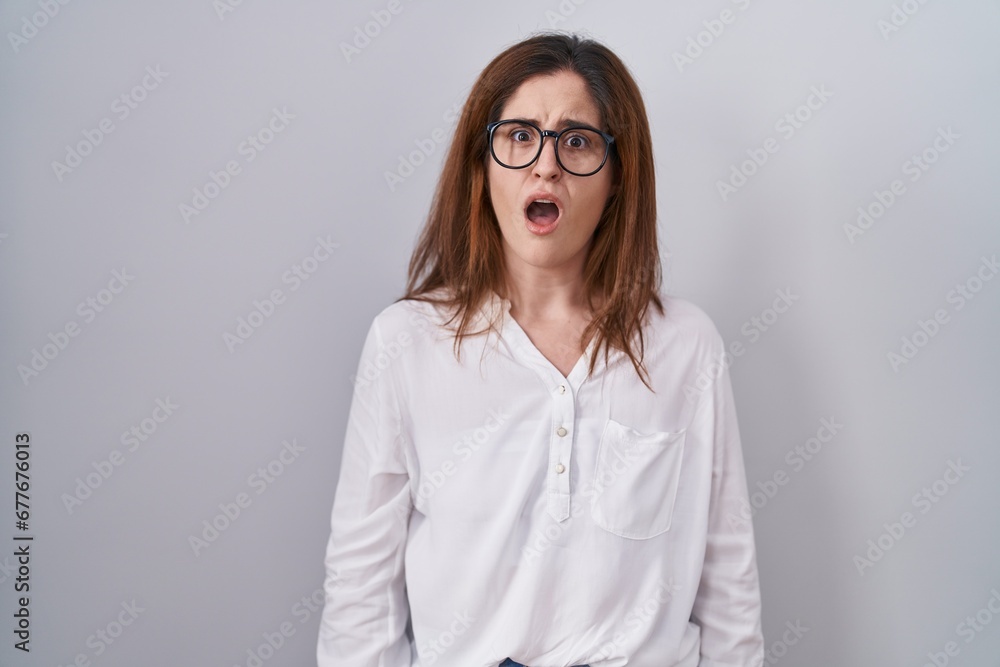 Brunette woman standing over white isolated background in shock face, looking skeptical and sarcastic, surprised with open mouth Brunette woman standing over white isolated background in shock face, looking skeptical and sarcastic, surprised with open mouth