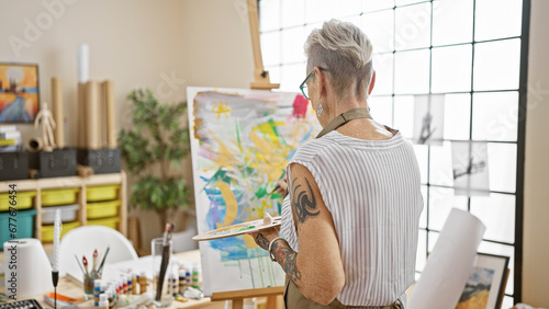 Mature grey-haired woman artist passionately drawing backwards, lost in her world of creativity at her cozy art studio. photo