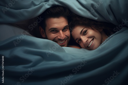 Cute husband and wife lying on the bed peeking out from under the blanket and smiling