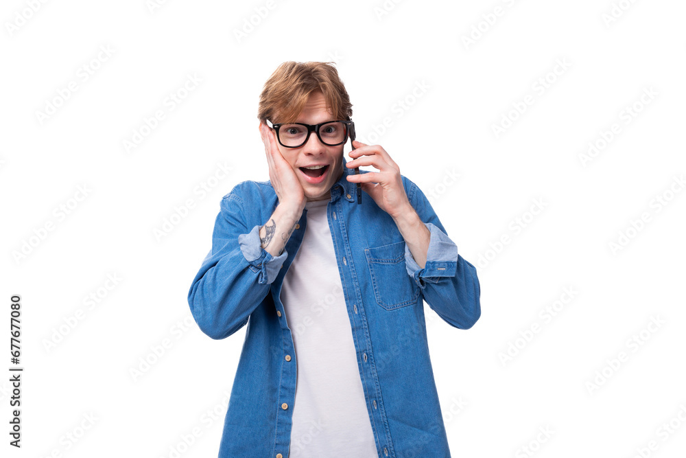 young surprised guy with red hair in a denim shirt chatting on the phone young surprised guy with red hair in a denim shirt chatting on the phone