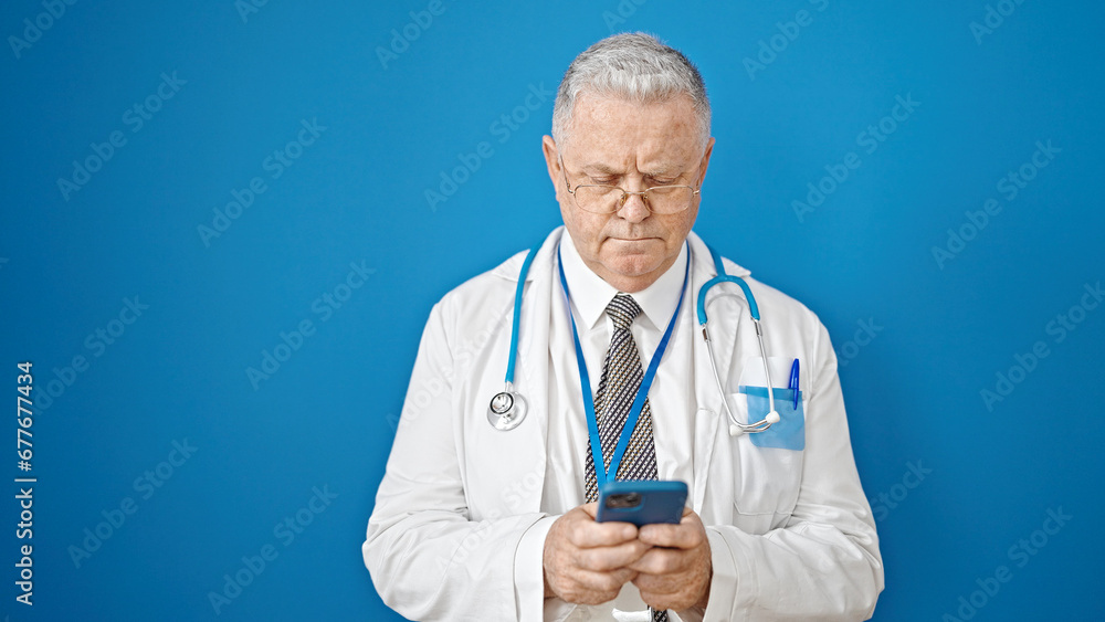 Middle age grey-haired man doctor using smartphone over isolated blue background Middle age grey-haired man doctor using smartphone over isolated blue background