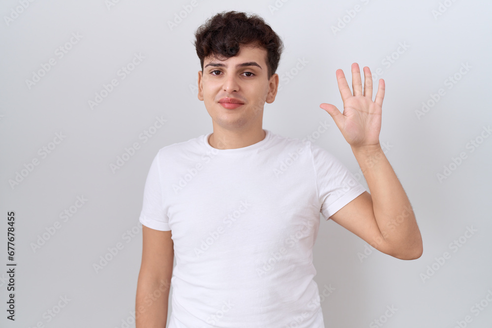 Young non binary man wearing casual white t shirt showing and pointing up with fingers number five while smiling confident and happy. Young non binary man wearing casual white t shirt showing and pointing up with fingers number five while smiling confident and happy.