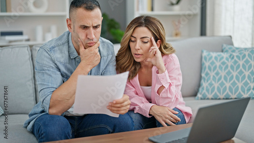 Man and woman couple using laptop reading document at home