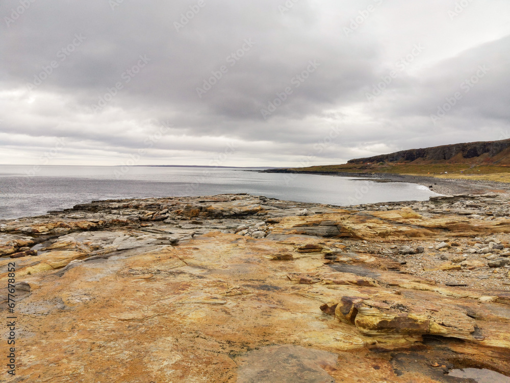 The shore of red stones next to the rocks are Two Brothers on the Fishing Peninsula. The picturesque shore of the harsh Barents Sea. The North of Russia. The Kola Peninsula. The Arctic The shore of red stones next to the rocks are Two Brothers on the Fishing Peninsula. The picturesque shore of the harsh Barents Sea. The North of Russia. The Kola Peninsula. The Arctic