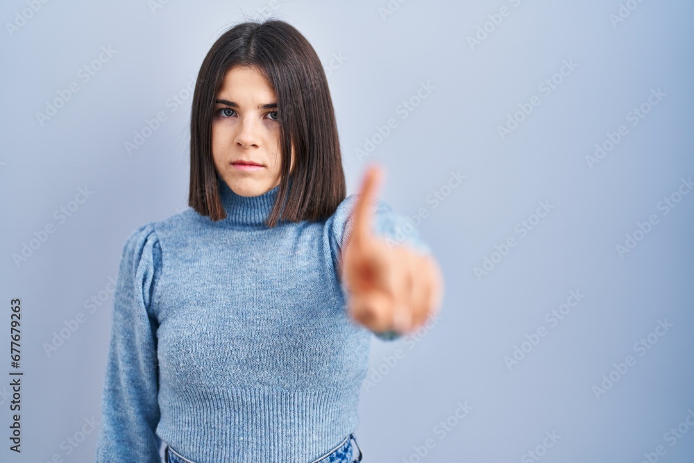 Young hispanic woman standing over blue background pointing with finger up and angry expression, showing no gesture Young hispanic woman standing over blue background pointing with finger up and angry expression, showing no gesture