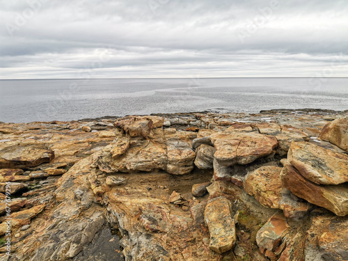 The shore of red stones next to the rocks are Two Brothers on the Fishing Peninsula. The picturesque shore of the harsh Barents Sea. The North of Russia. The Kola Peninsula. The Arctic