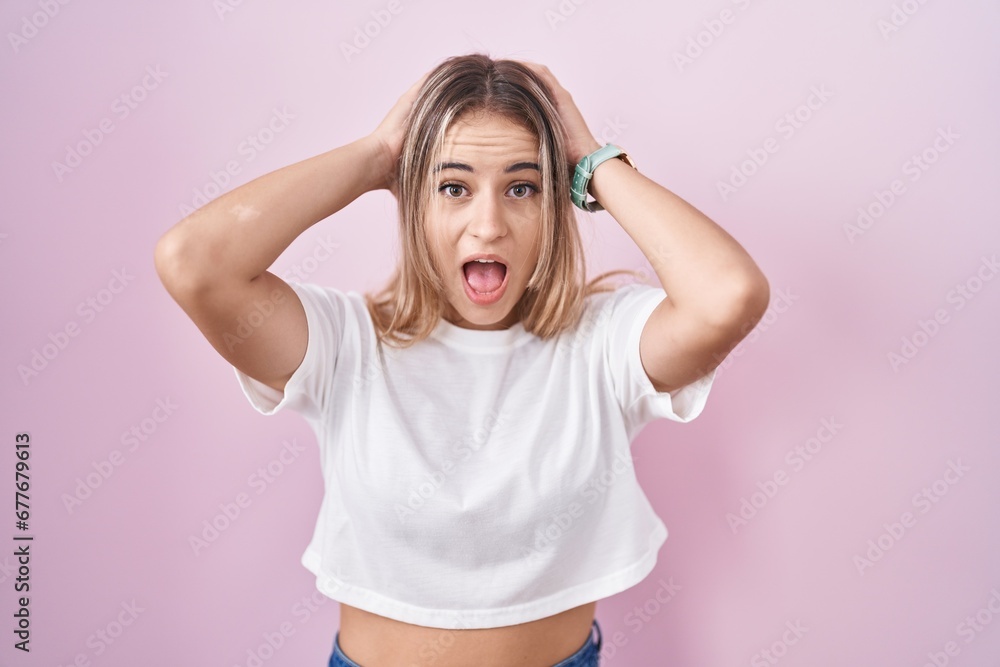 Young blonde woman standing over pink background crazy and scared with hands on head, afraid and surprised of shock with open mouth Young blonde woman standing over pink background crazy and scared with hands on head, afraid and surprised of shock with open mouth