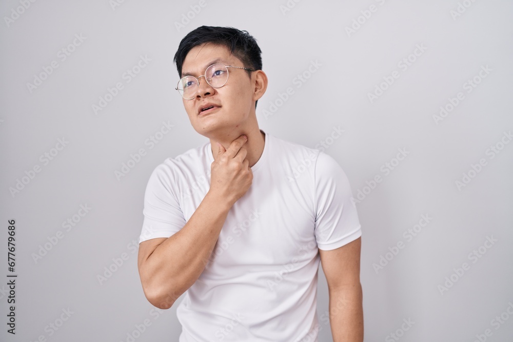 Young asian man standing over white background touching painful neck, sore throat for flu, clod and infection Young asian man standing over white background touching painful neck, sore throat for flu, clod and infection