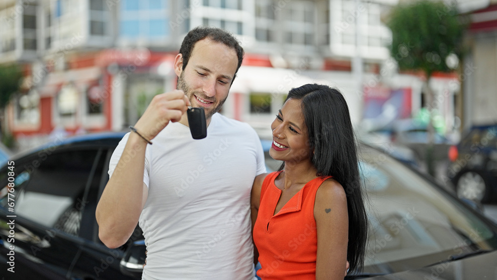 Beautiful couple hugging each other holding key of new car smiling at street Beautiful couple hugging each other holding key of new car smiling at street