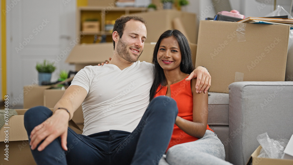 Beautiful couple hugging each other sitting on floor smiling at new home Beautiful couple hugging each other sitting on floor smiling at new home