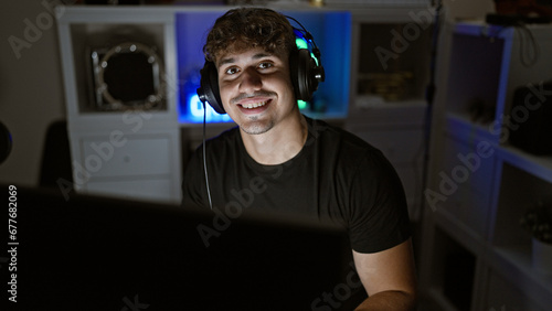 Engaging shot, smiling young hispanic man, a confident gamer and streamer, playing video game on computer in gaming room at night © Krakenimages.com