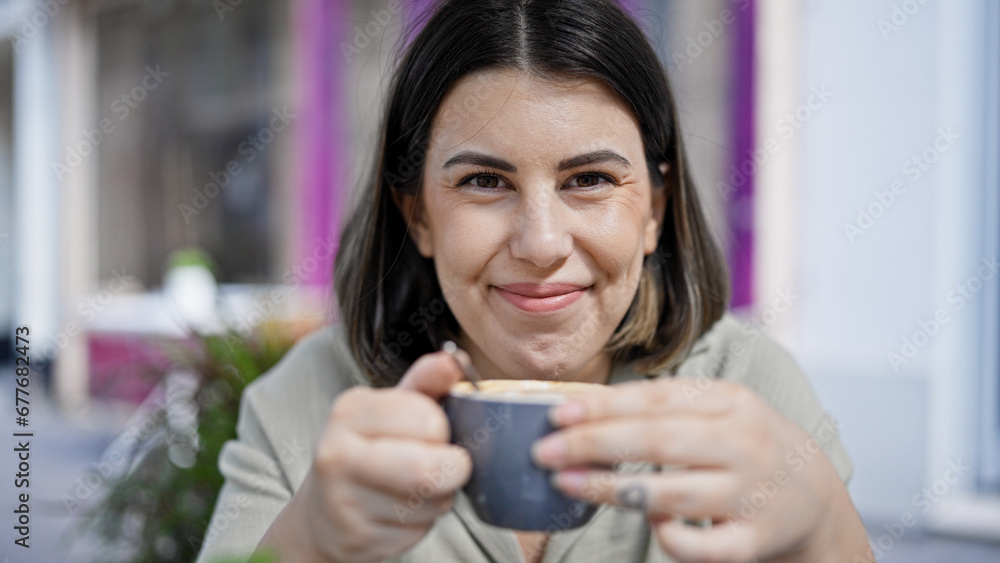 Young beautiful hispanic woman drinking coffee sitting on the table at outdoors cafeteria Young beautiful hispanic woman drinking coffee sitting on the table at outdoors cafeteria