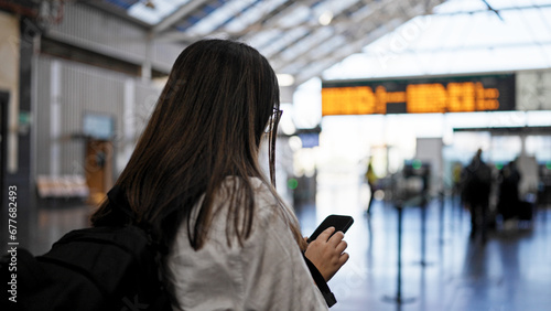 Young beautiful hispanic woman looking at train schedule on smartphone at train station