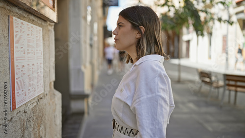 Young beautiful hispanic woman reading restaurant menu at the street