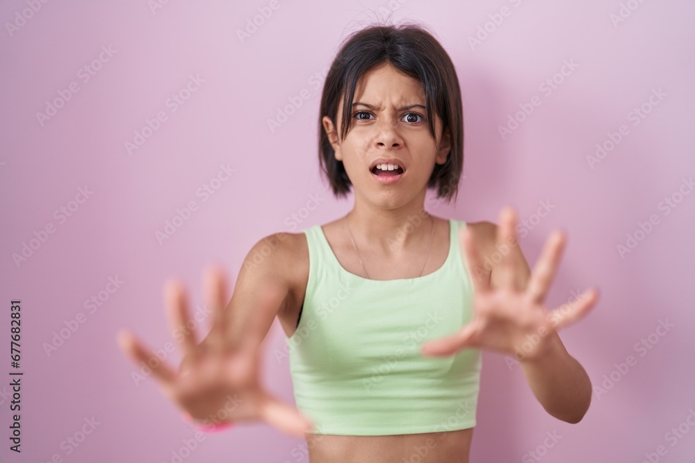 Young girl standing over pink background afraid and terrified with fear expression stop gesture with hands, shouting in shock. panic concept. Young girl standing over pink background afraid and terrified with fear expression stop gesture with hands, shouting in shock. panic concept.