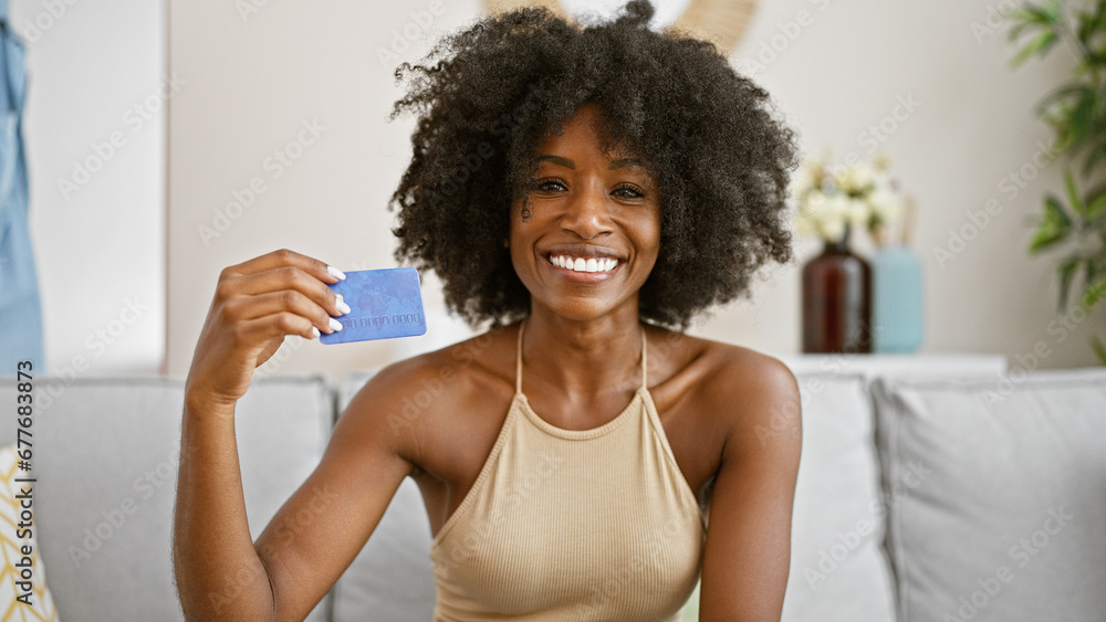 African american woman holding credit card sitting on sofa at home African american woman holding credit card sitting on sofa at home