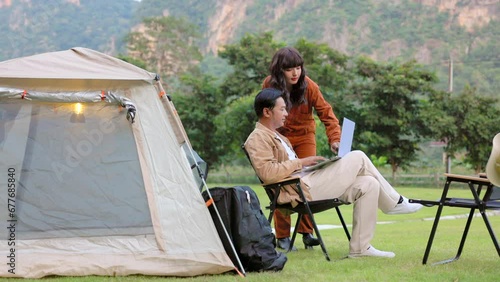 Happy asian couple planning road trip map next destination on laptop with internet connection at natural park.
