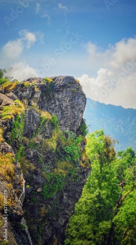  landscape featuring a rocky mountain cliff with trees. The mountain is surrounded by clouds in the sky