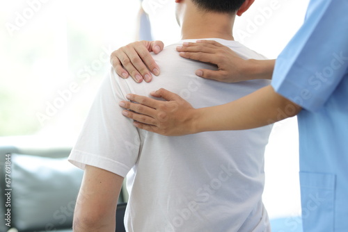 Doctor diagnosing man's shoulder pain in hospital examination room. Nurse doing massage and physiotherapy to treat patient's shoulder. photo