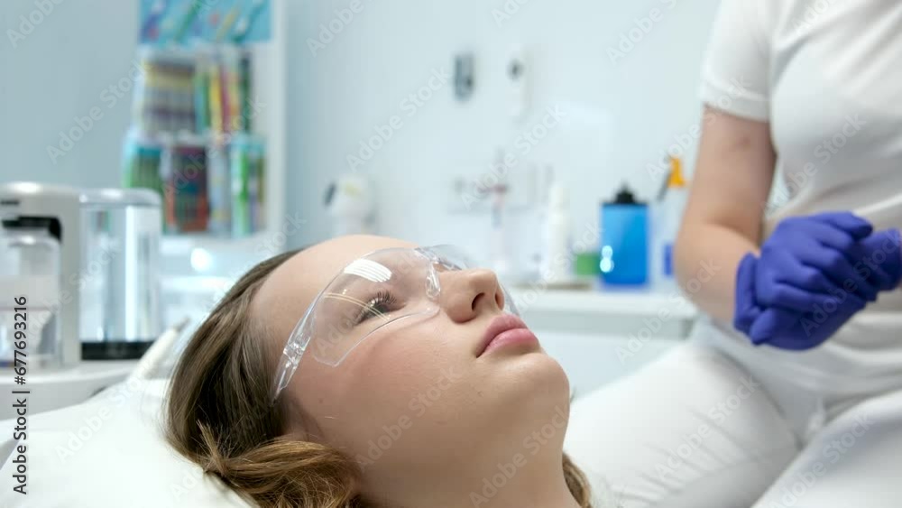 Cute girl in a patient bib in a dental clinic. Dentist with an assistant are examining her teeth with a help of a dental bur with a mirror and an air polisher. Video recording. High quality 4k footage Cute girl in a patient bib in a dental clinic. Dentist with an assistant are examining her teeth with a help of a dental bur with a mirror and an air polisher. Video recording. High quality 4k footage