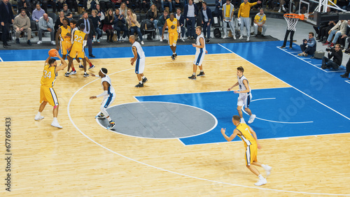 TV Broadcast Style Footage Of Basketball Championship in an Arena. Yellow Team Passing the Ball Between Teammates, Forward Player Aiming to Score a Two-Point Goal From a Distance. Sports Channel. photo