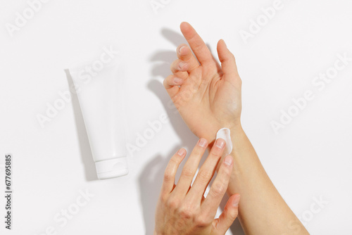 female applies a smear of white cream on her hand with her fingers and mockup of a tube lying next to her on a white isolated background. Concept of beauty and skin care products for hands and face