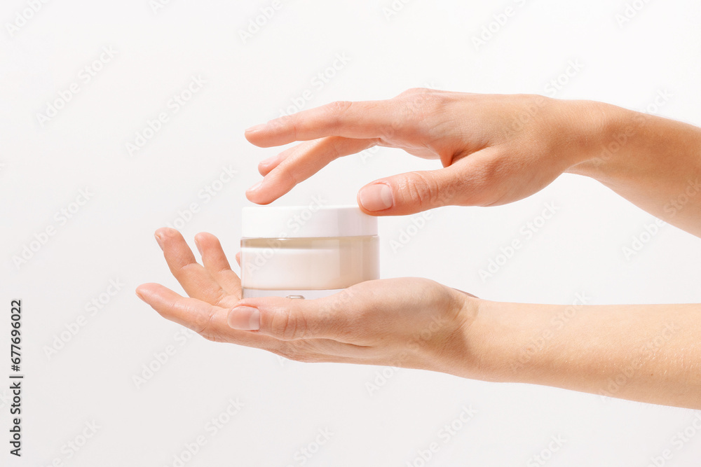 Female fragile hands holding glass transparent mockup jar of face cream on white isolated background. The concept of presenting a new beauty product, skin care, moisturizing and nutrition Female fragile hands holding glass transparent mockup jar of face cream on white isolated background. The concept of presenting a new beauty product, skin care, moisturizing and nutrition