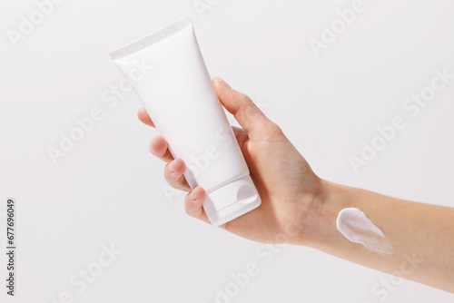 Close-up of a female hand holding a white mockup blank tube of cream on a white isolated background. Beauty products, cosmetologist and facial skin care concept. photo