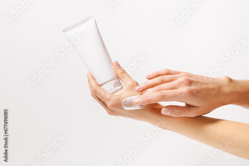 Female hand holding white mockup tube of cream or lotion and applying on skin with fingers on white isolated background. Beauty products, face cream texture, skin care concept. photo