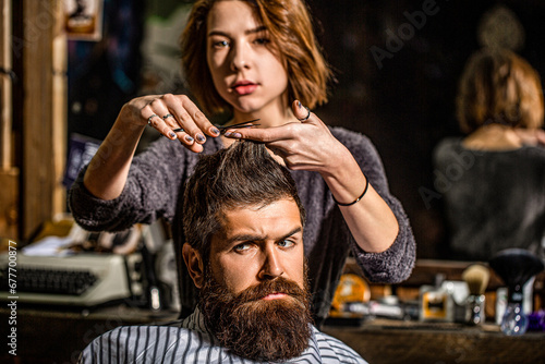 Working hair scissors. Professional barber girl cutting hair of bearded man. He is getting haircut at barbershop. Barbershop, beauty salon. Beard man in barbershop. Barber scissors, barber shop