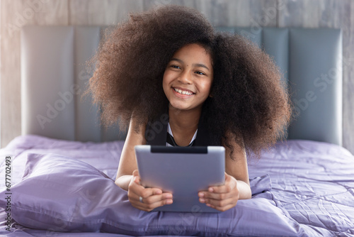 Happy african black afro child teen girl smiling lay on bed with tablet computer learning education at home with technology digital device.