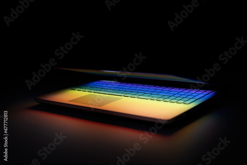 half closed laptop on dark table with colourful light reflection on keyboard photo