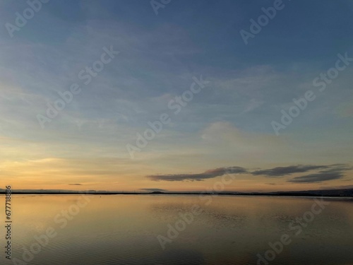 Breathtaking view from the shore of a blue and orange cloudy sunset sky over the ocean © Wirestock