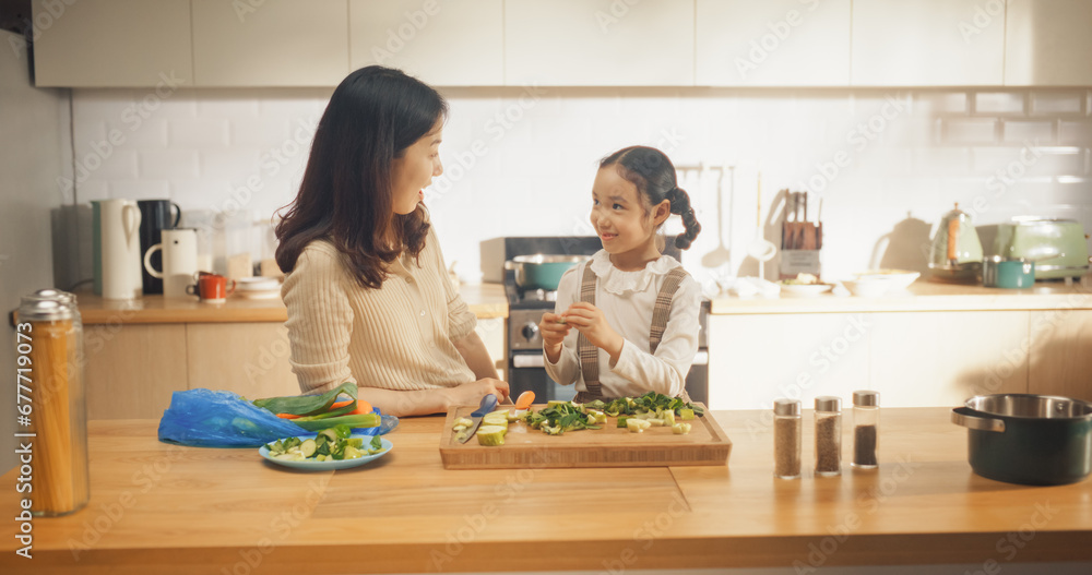 In the Kitchen: Korean Mother and Cute Little Daughter Cooking Together Healthy Dinner. Mother Teaches Little Girl Healthy Habits and How to Cut Vegetables for Salad. Cute Child Helping Her Parent
