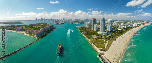Commercial container ship entering Miami port harbor through main channel near South Beach. Luxurious hotels and residential buildings on waterfront and high skyscraper towers of downtown in distance
