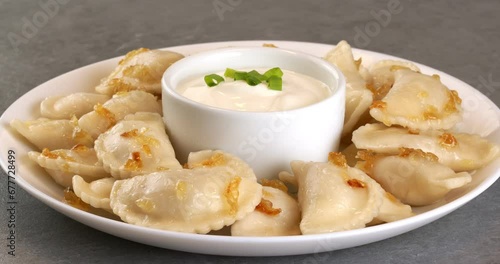 Dumplings with fried onions and bowl with sour cream. Varenyky, vareniki, pierogi, pyrohy with filling.
Close-up footage on the rotating table. photo