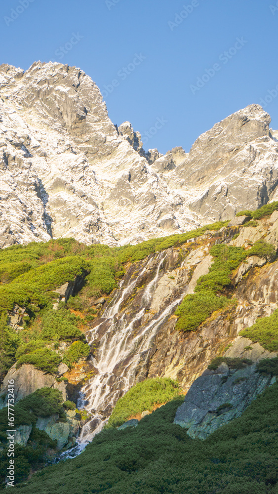 Waterfall on the hills of the  rocky and snowy mountains on a sunny day