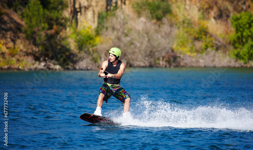 Man, wakeboarding and water with helmet, sport and fitness for speed on vacation in summer sunshine. Person, athlete and ski with rope for safety on lake, sea or river for training, exercise or waves