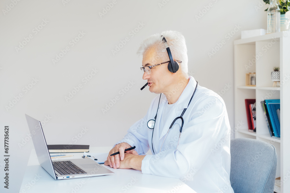 Middle aged male doctor using headset and laptop for online video call consulting of patient. Telemedicine concept for domestic health treatment. Online remote medical appointment. Medical technology. Middle aged male doctor using headset and laptop for online video call consulting of patient. Telemedicine concept for domestic health treatment. Online remote medical appointment. Medical technology.