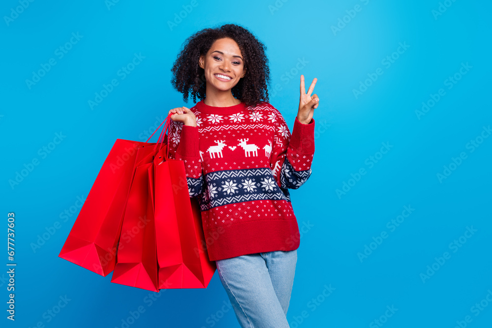 Photo of adorable lovely girl wear stylish clothes hand hold packages purchase v-sign isolated on blue color background