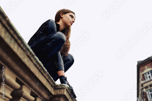 Woman, leather catsuit and roof in city for superhero character, thinking and vigilante. Girl, cosplay clothes and fashion for criminal, spy or agent on balcony for mystery, vision or mission photo
