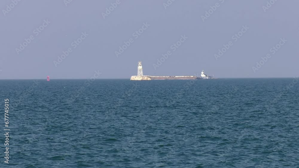 Barge and towboat on Lake Michigan near Racine. Long wide shot shows the boat and barge passing behind an outer beacon and buoy on the lake. Shot on a smoky day as wildfire smoke moves in from Canada. Barge and towboat on Lake Michigan near Racine. Long wide shot shows the boat and barge passing behind an outer beacon and buoy on the lake. Shot on a smoky day as wildfire smoke moves in from Canada.