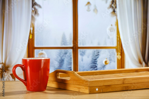 Red mug of hot drink and winter christmas background of window sill. Empty space for your decoration. 