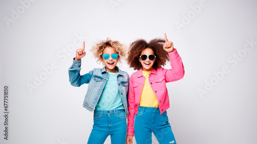 Dos niñas adolescentes Gen Z, vestidas a la moda, con gafas, señalando con su dedo, aisladas en un fondo blanco  photo