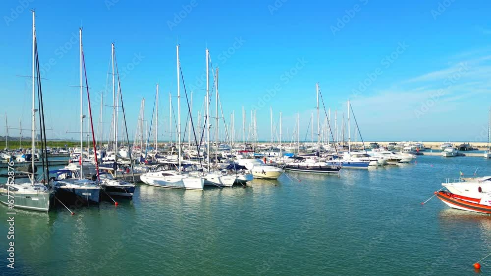 Energizing aerial pedestal up shot from the Port of Porto San Giorgio with the minutely rippling waters of the Adriatic Sea washing the docked boats, with breakwaters, meadows, buildings, skyscrapers Energizing aerial pedestal up shot from the Port of Porto San Giorgio with the minutely rippling waters of the Adriatic Sea washing the docked boats, with breakwaters, meadows, buildings, skyscrapers