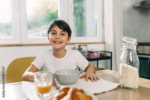 Cute young boy sitting by the kitchen table and having oats for breakfast. photo